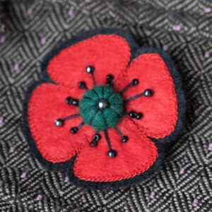 Red felt poppy flower on black background, Green felt and bead feature stamen.
